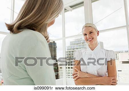 Stock Photography - Two businesswomen talking in office. Fotosearch