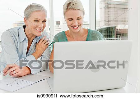 Stock Image - Two businesswomen using laptop in office. Fotosearch