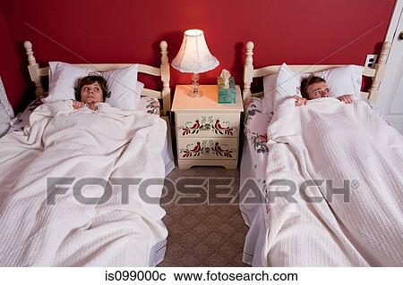 Stock Image - Young couple hiding under bedclothes. Fotosearch