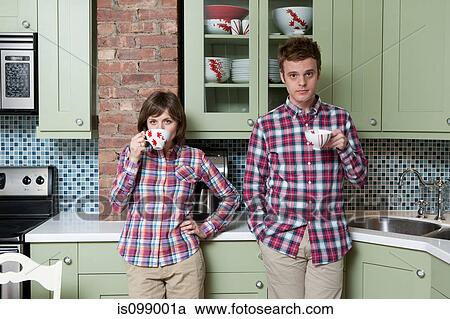 Stock Image - Young couple holding teacups in kitchen. Fotosearch