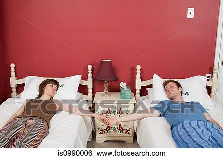 Young couple lying on single beds, holding hands View Large Photo Image Stock Photograph - Young couple lying on single beds, holding hands. Fotosearch