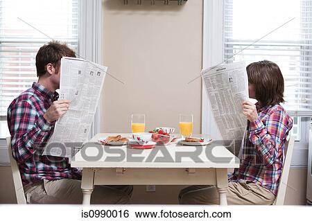Stock Photograph - Young couple reading newspapers at kitchen table. Fotosearch