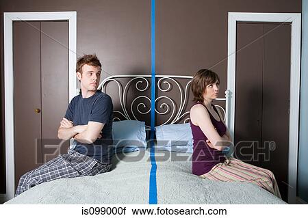 Young couple sitting on bed separated by blue line View Large Photo Image Stock Image - Young couple sitting on bed separated by blue line. Fotosearch