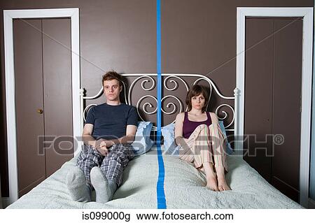 Young couple sitting on bed separated by blue line View Large Photo Image Stock Image - Young couple sitting on bed separated by blue line. Fotosearch