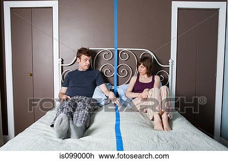 Young couple sitting on bed separated by blue line View Large Photo Image Stock Image - Young couple sitting on bed separated by blue line. Fotosearch