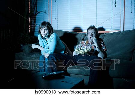 Young couple watching tv, man eating popcorn View Large Photo Image Stock Image - Young couple watching tv, man eating popcorn. Fotosearch