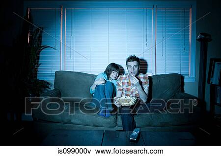 Young couple watching tv, man eating popcorn View Large Photo Image Stock Photo - Young couple watching tv, man eating popcorn. Fotosearch