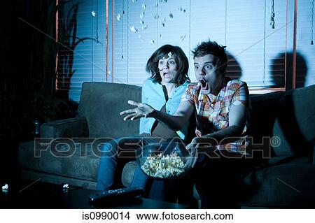 Young couple watching tv, man throwing popcorn View Large Photo Image Picture - Young couple watching tv, man throwing popcorn. Fotosearch