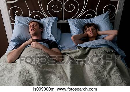 Picture - Young man snoring, woman covering ears. Fotosearch