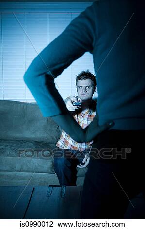 Stock Image - Young man watching tv, woman blocking view. Fotosearch