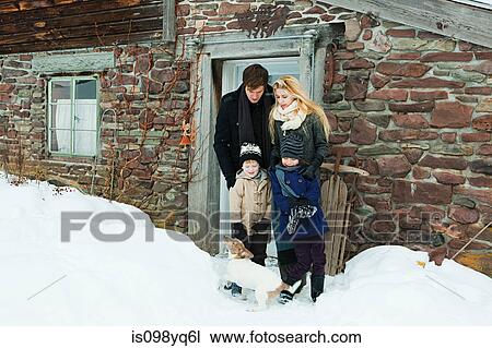 Stock Image - Family outside rustic house in snow. Fotosearch