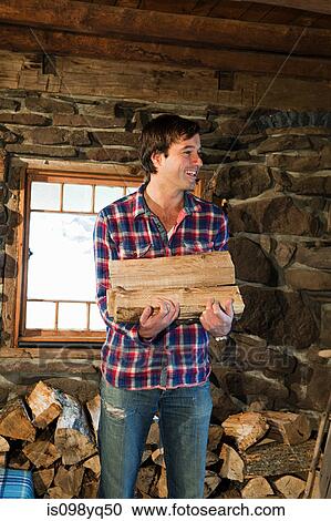 Mid adult man holding logs in rustic house View Large Photo Image Stock Image - Mid adult man holding logs in rustic house. Fotosearch