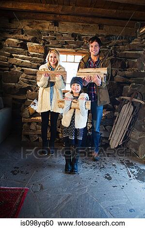Stock Image - Portrait of family in rustic house holding logs. Fotosearch