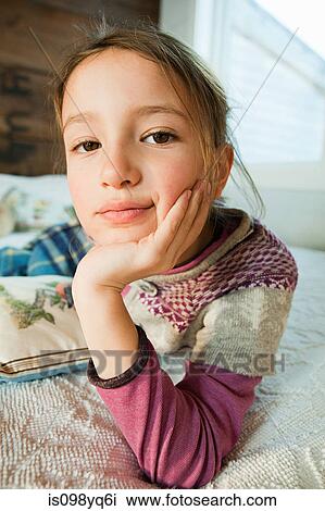 Stock Image - Young girl lying on bed looking at camera. Fotosearch