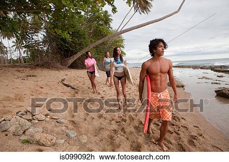 Stock Image - Four young friends carrying surfboards on beach. Fotosearch