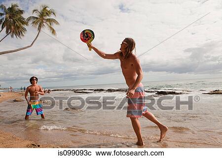 Stock Image - People on beach, men playing bat and ball game. Fotosearch