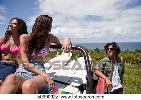 Stock Photo - Three young friends in off road vehicle with surfboards. Fotosearch