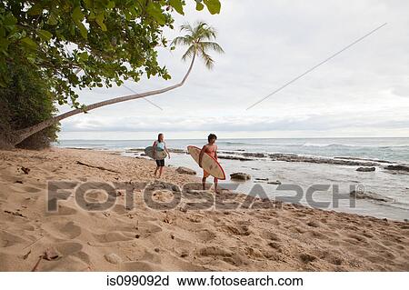 Stock Image - Two men carrying surfboards on beach. Fotosearch