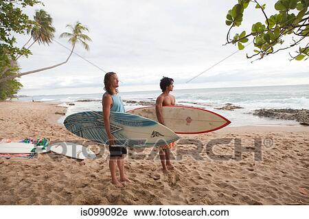 Two men holding surfboards on beach View Large Photo Image Stock Image - Two men holding surfboards on beach. Fotosearch