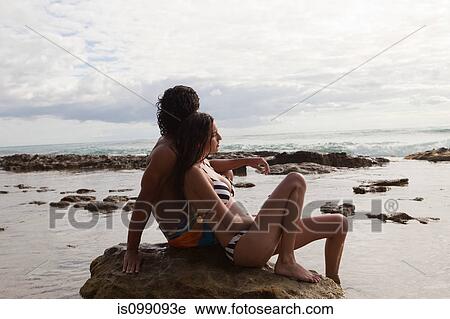Young couple sitting on rock, side view View Large Photo Image Stock Image - Young couple sitting on rock, side view. Fotosearch