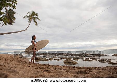 Stock Image - Young woman holding surfboard, portrait. Fotosearch
