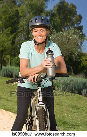 Mature woman cyclist wearing helmet and holding bottle View Large Photo Image Stock Photo - Mature woman cyclist wearing helmet and holding bottle. Fotosearch