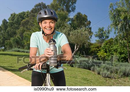 Mature woman cyclist wearing helmet and holding bottle View Large Photo Image Stock Photo - Mature woman cyclist wearing helmet and holding bottle. Fotosearch