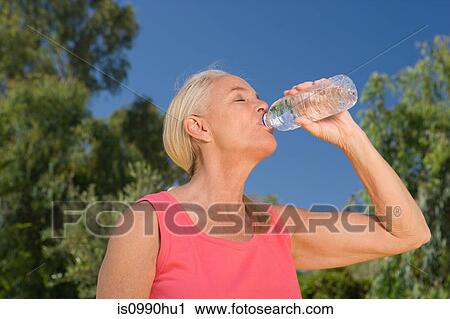 Stock Image - Mature woman runner drinking water. Fotosearch
