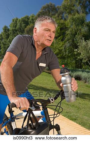 Stock Image - Senior male cyclist holding water bottle. Fotosearch