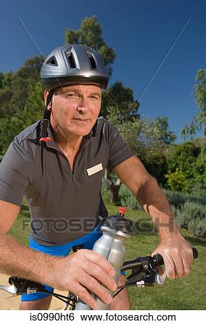 Stock Photograph - Senior male cyclist wearing helmet and holding bottle. Fotosearch