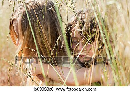Stock Image - Girl giving friend piggy back in field, close up. Fotosearch