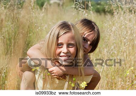 Stock Photo - Girl giving friend piggy back in field. Fotosearch