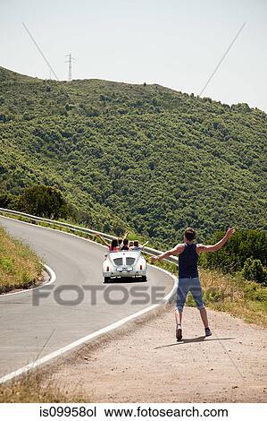 Stock Image - Convertible car driving past hitchhiker. Fotosearch