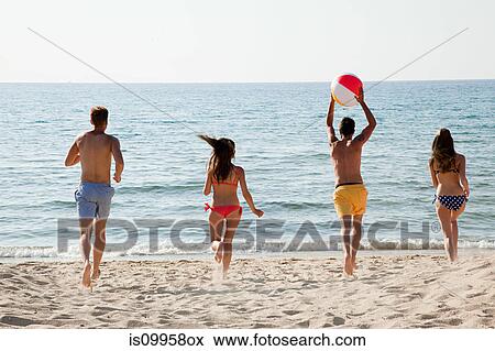 Stock Photo - Four people playing with beach ball on beach. Fotosearch