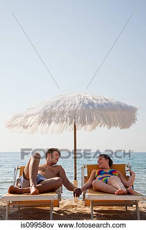 Young couple on sun loungers holding hands View Large Photo Image Stock Photo - Young couple on sun loungers holding hands. Fotosearch
