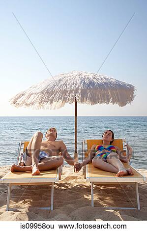 Young couple on sun loungers holding hands View Large Photo Image Stock Photograph - Young couple on sun loungers holding hands. Fotosearch