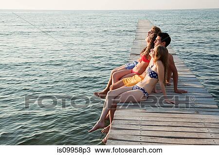 Stock Image - Young friends sitting on jetty. Fotosearch