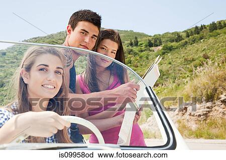 Stock Image - Young friends with convertible car looking at map. Fotosearch