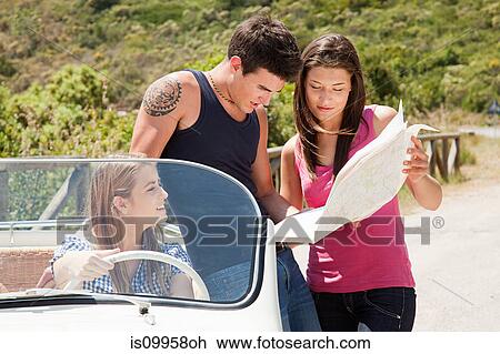 Stock Image - Young friends with convertible car looking at map. Fotosearch