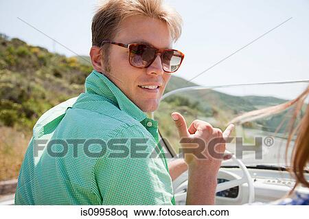 Stock Photography - Young man wearing sunglasses driving convertible car. Fotosearch
