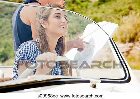 Stock Image - Young people with convertible car looking at map. Fotosearch
