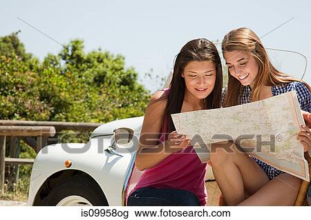 Stock Image - Young women with convertible car looking at map. Fotosearch