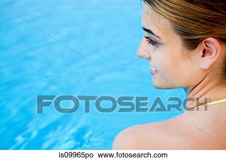 Picture - Portrait of young woman by swimming pool, view over shooulder. Fotosearch
