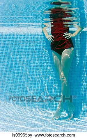 Stock Photo - Woman standing with hands on hips in swimming pool, underwater view. Fotosearch