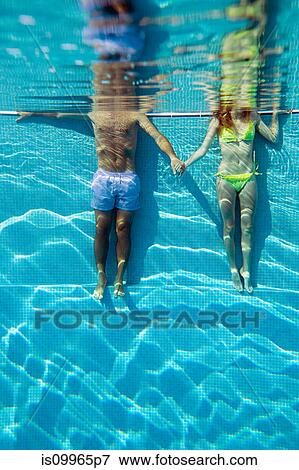 Stock Photo - Young couple holding hands in swimming pool, underwater view. Fotosearch