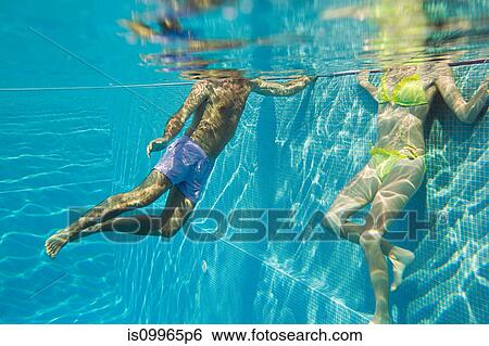 Stock Photograph - Young couple in swimming pool, underwater view. Fotosearch