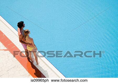 Stock Image - Young couple standing at poolside. Fotosearch