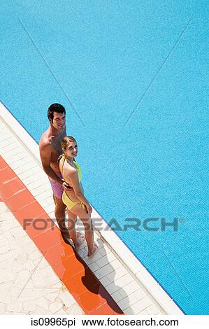 Young couple standing at poolside View Large Photo Image Stock Image - Young couple standing at poolside. Fotosearch