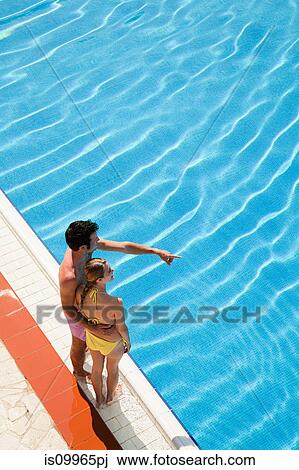 Young couple standing at poolside View Large Photo Image Stock Image - Young couple standing at poolside. Fotosearch