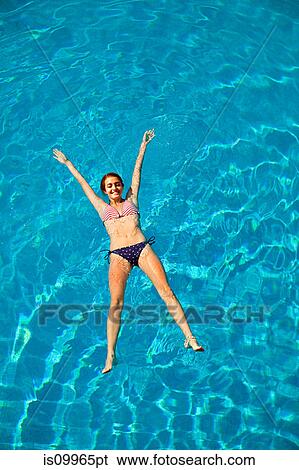 Stock Photograph - Young woman floating in swimming pool. Fotosearch